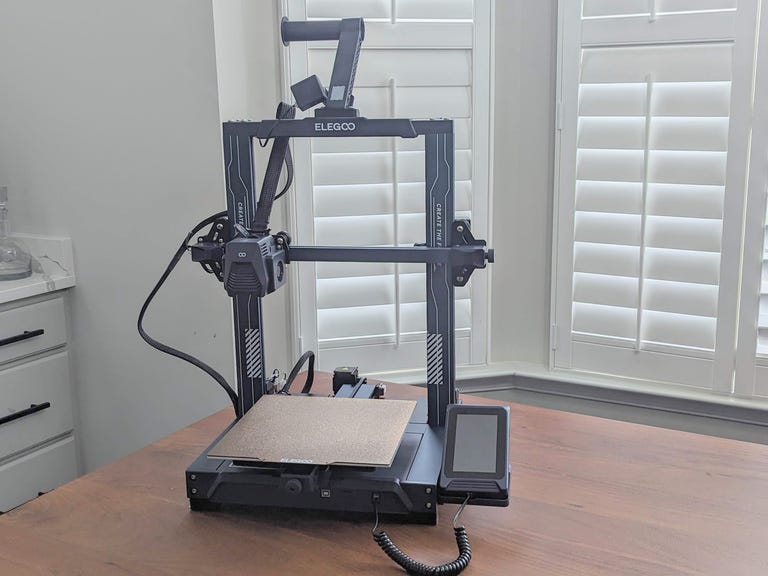 Blue 3d printer on a table with window shutters behind it